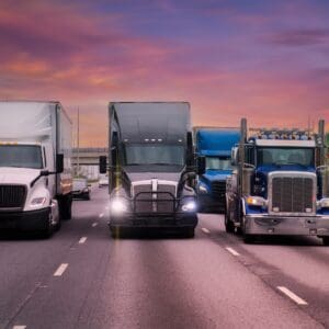 Three semi-trucks on highway at sunset.
